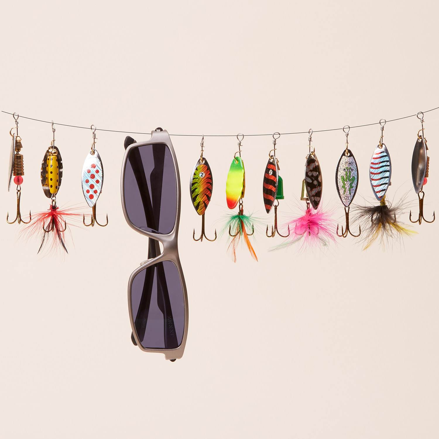 Sunglasses and various colorful fishing lures with hooks and feathers hanging on a string.