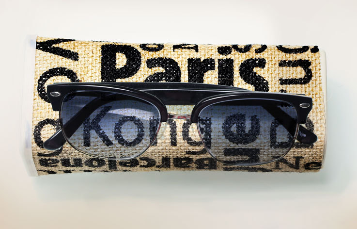 Black sunglasses with round frames on a fabric case with text: "Paris, Kong, New York."