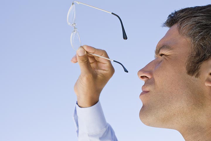 Man squinting and closely inspecting a pair of eyeglasses held in his hand.