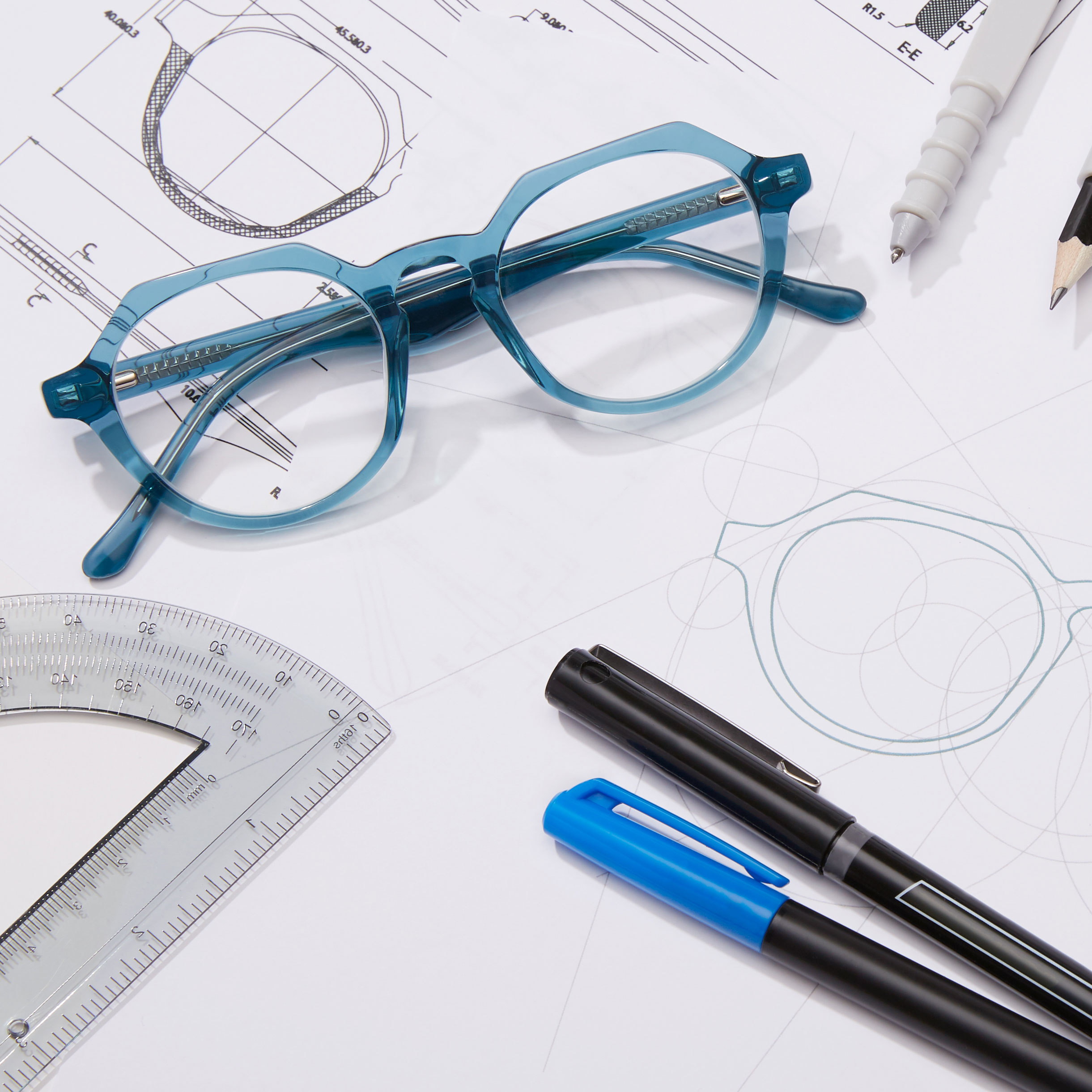 Blue-framed eyeglasses on technical drawings with pens, pencil, and ruler.