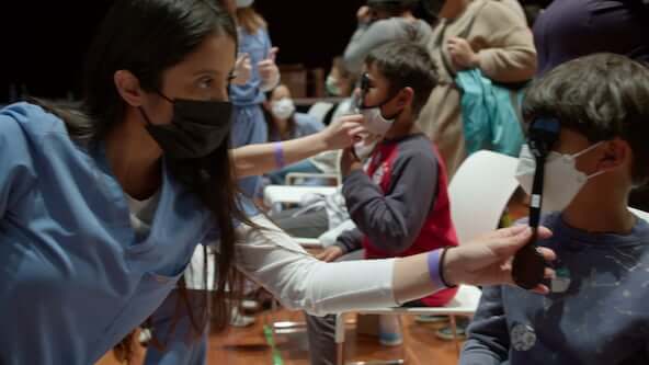 Healthcare worker checks vision of seated child using a handheld vision screening device.