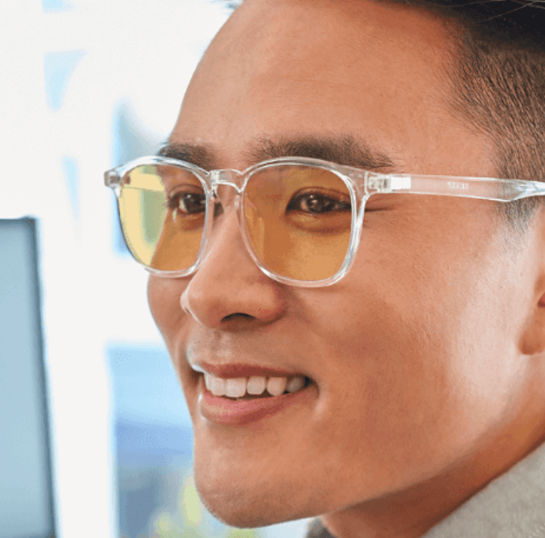 Clear frame eyeglasses with yellow tinted lenses worn by a smiling individual.