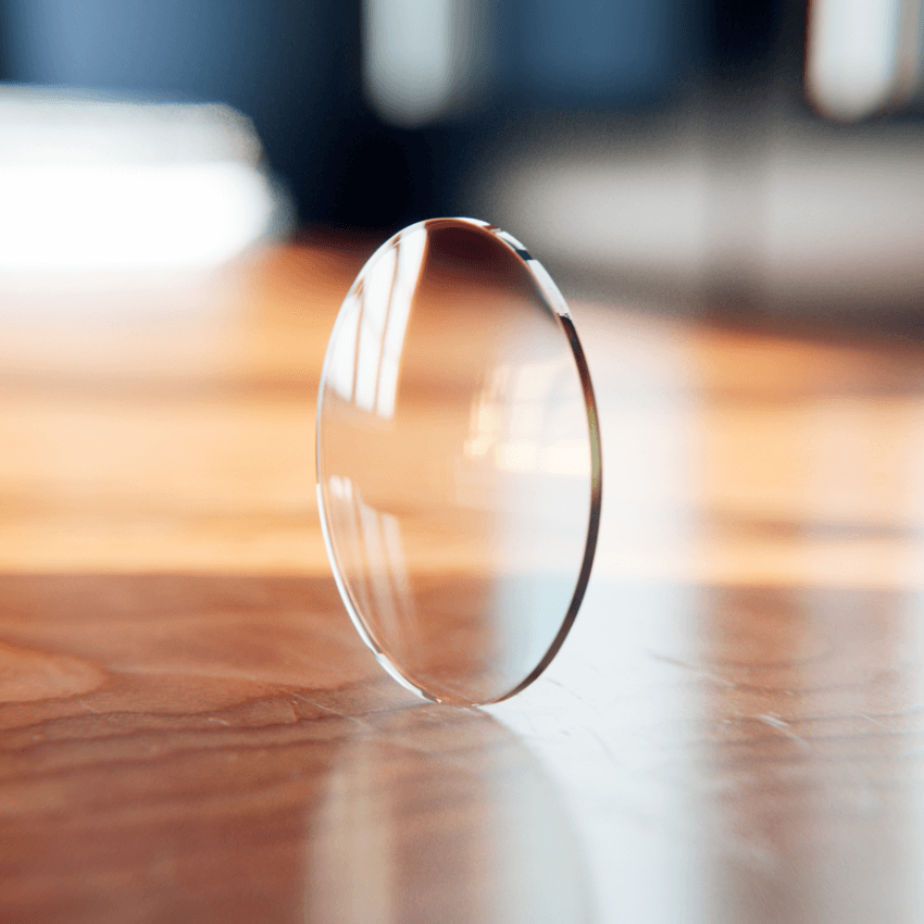 Single transparent glass lens standing upright on a wooden surface.