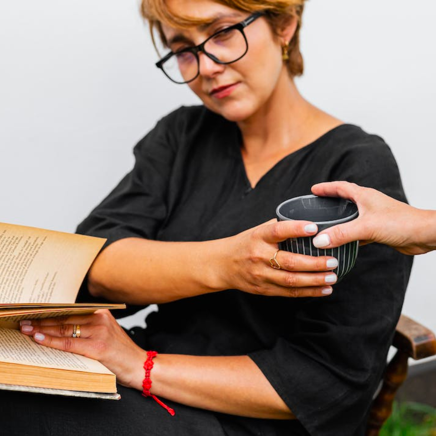 Woman in black dress holding a ceramic cup and reading a book.