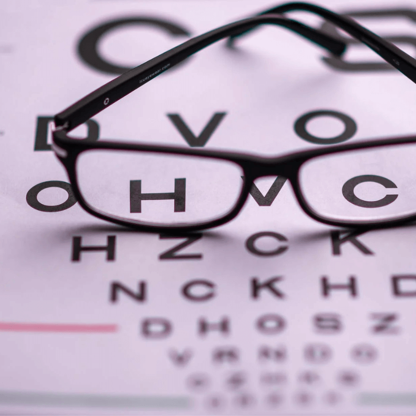 Black rectangular eyeglasses placed on a Snellen eye chart with letters DVO OHVC HZCK NCKHD DHOSZ.