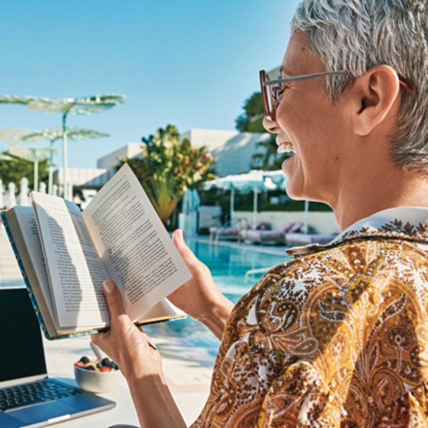 Person in sunglasses reading a book outdoors.