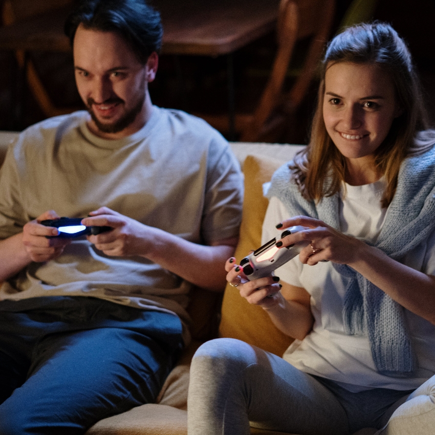 Two people sitting on a couch, playing video games with controllers.