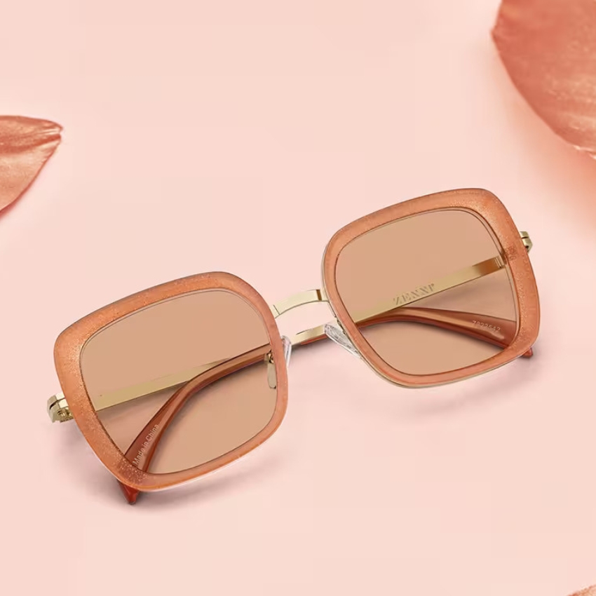 Square, peach-colored sunglasses with brown lenses and gold accents on pink background. Text on inside arm: "ZASNT".