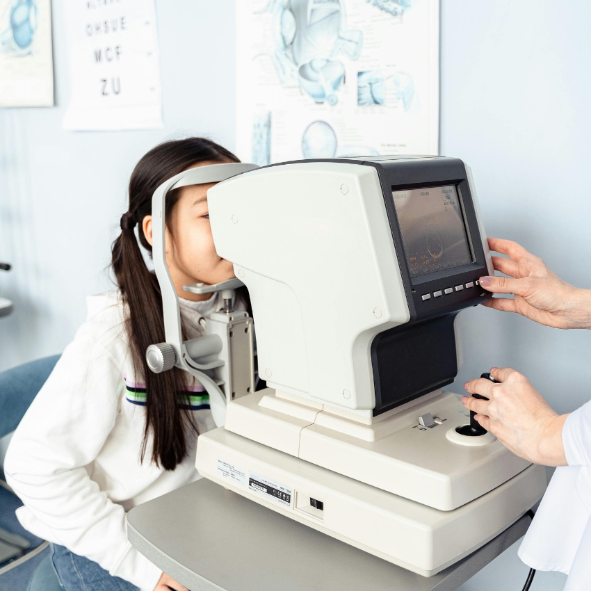 Optometry machine being used to examine a child's eye with a technician adjusting the device settings.