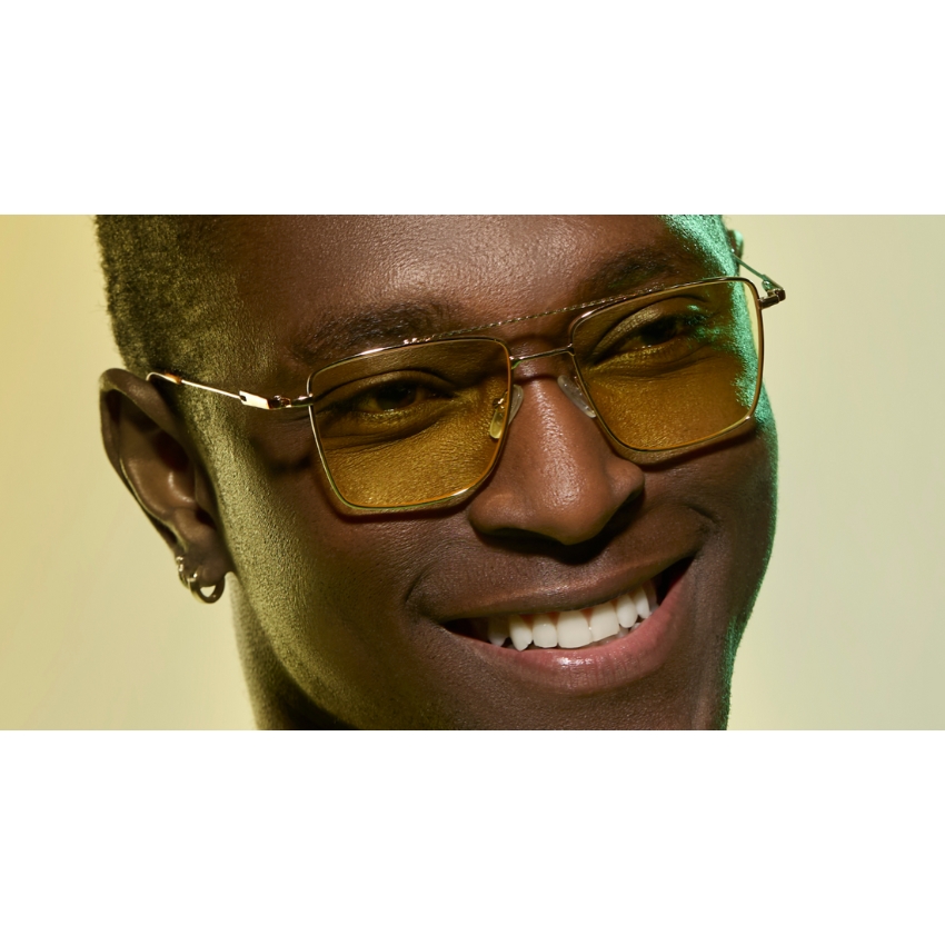 Man wearing gold-rimmed, yellow tinted rectangular sunglasses with a smile.