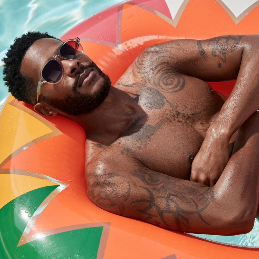 Man wearing sunglasses, lying on an orange and green pool float with arms crossed.