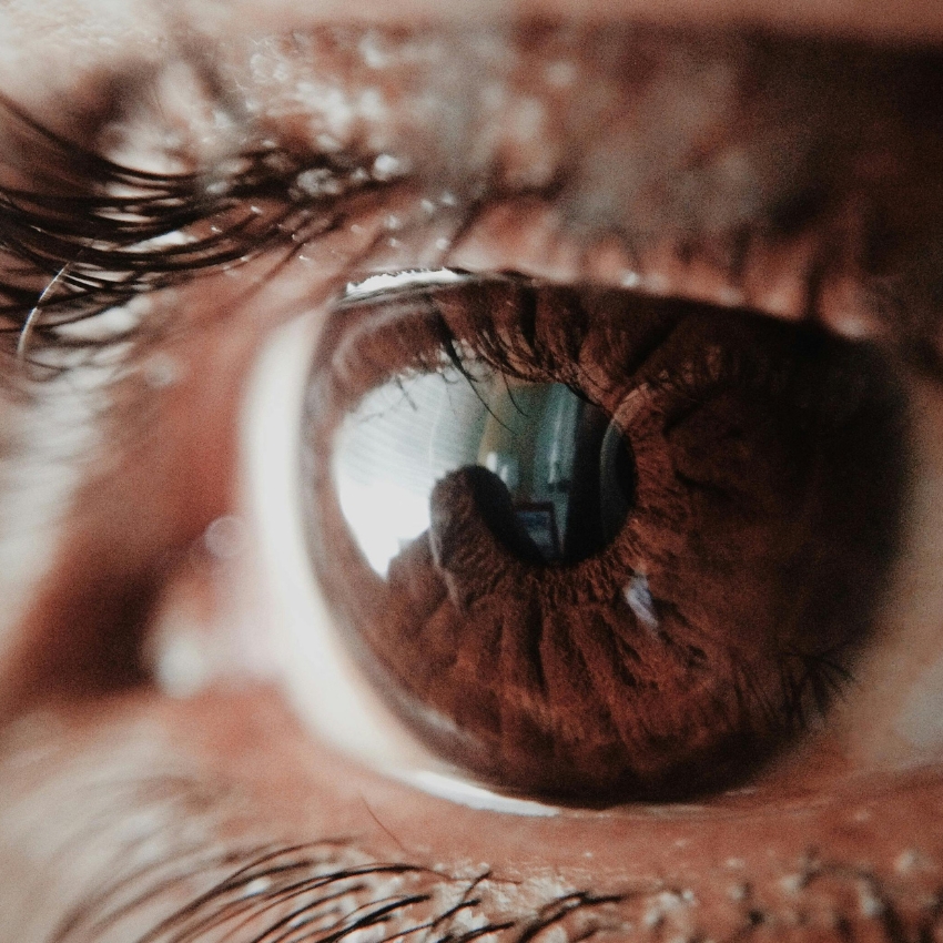 Close-up of a human eye, highlighting the brown iris and detailed reflection in the pupil.