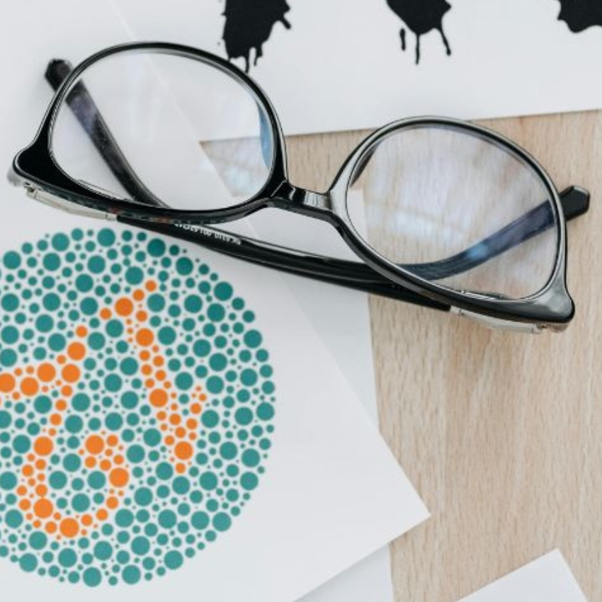 Eyeglasses resting on a table with a color blindness test card showing the number 6.