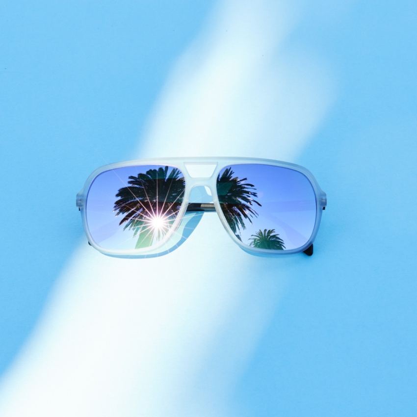 Stylish sunglasses with mirrored lenses reflecting palm trees and sunlight.