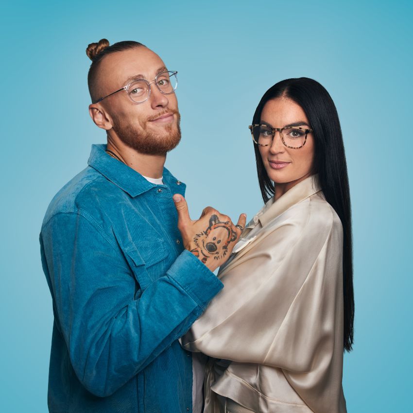 Man and woman wearing stylish eyeglasses; he wears a blue jacket, and she wears a cream robe.