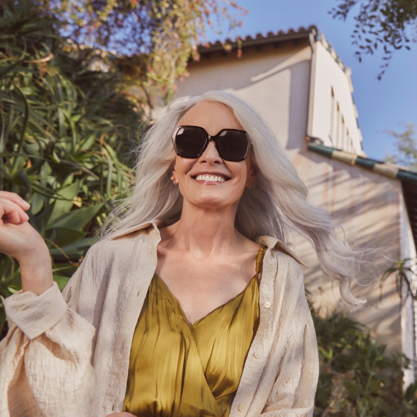 Woman wearing black sunglasses, a light beige cardigan, and a green dress.