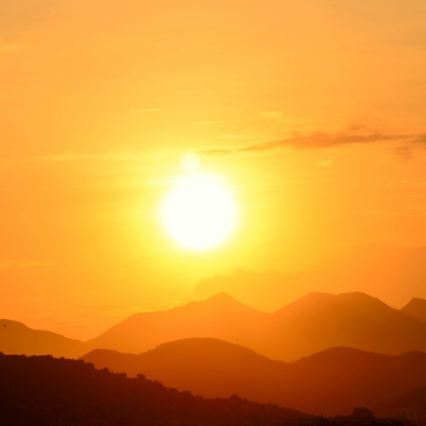 Bright sun setting over a landscape of orange-tinted mountains.