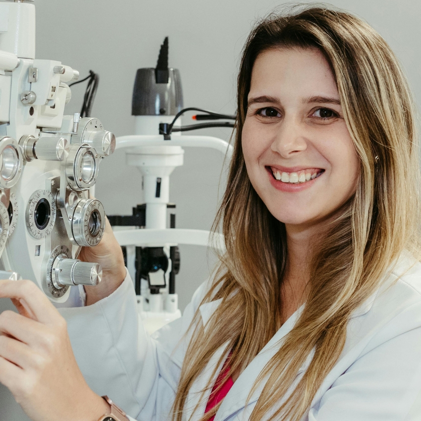 Woman operating an optometry phoropter while smiling.