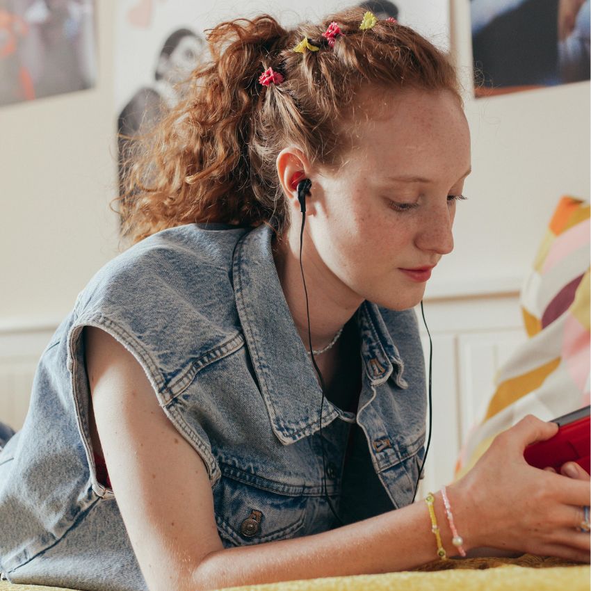 Teenager wearing earbuds while looking at a red smartphone.
